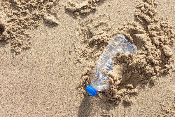 Environmental pollution. Human waste throwing away junk bottle on the sand, bring the sea to rot, closeup. Beach garbage environmental damage causing global warming