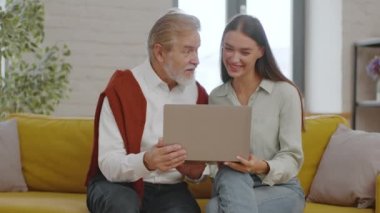 Yaşlılar ve dijitalleşme. Genç, güzel bir kadın, dizüstü bilgisayarını yaşlı gri saçlı dedesine gösteriyor. Ona evde internet kullanmayı öğretiyor. İzleme çekimi, yavaş çekim, serbest alan.