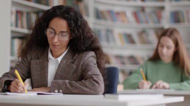 Offline schooling. Group of smart clever young women students studying at college classroom, listening to teacher and writing notes, tracking shot, slow motion, free space