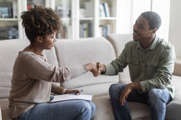 Mental health, therapy, psychological assistance. Smiling happy cheerful millennial black guy shaking therapist attractive young woman hand, patient thankful for helpful session, copy space