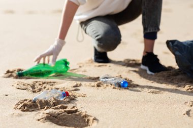 Volunteer woman picking plastic bottles into trash plastic bag for cleaning the beach and coastal zone, cleaning up garbage. Ecology concept and World Environment Day