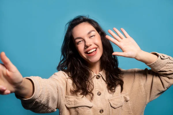 Happy pretty millennial european female student taking selfie and waving hand at camera, isolated on blue background, close up, studio. Social networks, blog video shooting, video call, ad and offer