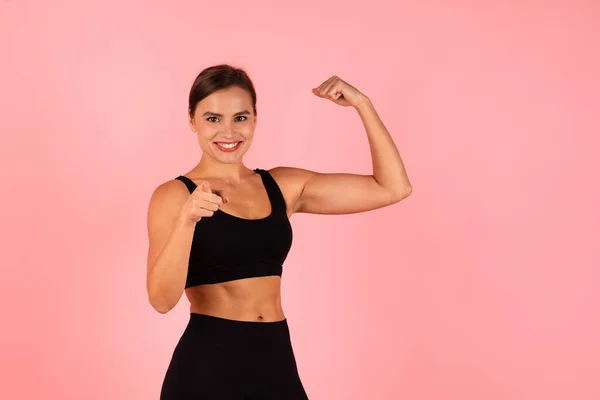 You Can Do It. Motivated Sporty Woman Showing Her Biceps And Pointing At Camera, Smiling Fit Female In Sportswear Advertising Healthy Lifestyle While Standing Isolated On Pink Background, Copy Space