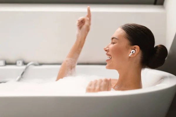 Cheerful Female Listening Music Wearing Earbuds Relaxing Bath Foam Singing — Stockfoto