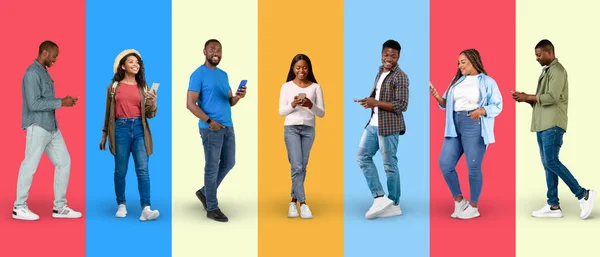 Cheerful young black people in casual chatting on smartphone, surfing in internet on colorful background, studio, panorama, full length. App and gadget for communication, work and social networks