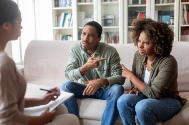 African american spouses young man and woman sitting on couch at family therapist office, pointing at one another, blaming each other in marriage problems while visiting psychologist, copy space