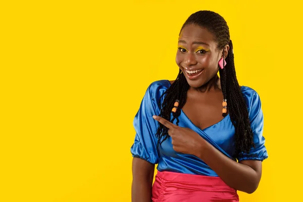 Braided Black Woman Pointing Finger Aside At Free Space For Text Advertising Great Offer Smiling To Camera Posing Over Yellow Background In Studio. Look There Concept