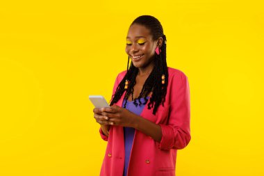 Mobile Application. Black Lady Using Phone Smiling Reading Message Standing On Yellow Background, Studio Shot. Happy Woman Browsing Internet And Using New App On Cellphone