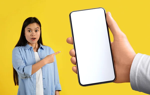Glad surprised funny young japanese female with open mouth, pointing finger at empty space isolated on yellow background, panorama, studio. Shocking ad and offer, amazed facial expression and emotions