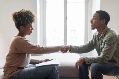 Mental health, therapy, psychological assistance. Side view of happy cheerful millennial black guy shaking therapist attractive young woman hand and smiling, thankful for helpful session, copy space