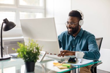 Happy black businessman in headset working on computer, making conference video call, having conversation with client online, customer service support helpline concept