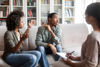 African american spouses young man and woman sitting on couch at family therapist office, fighting while visiting psychologist, angry black lady shouting at ignorant guy, copy space