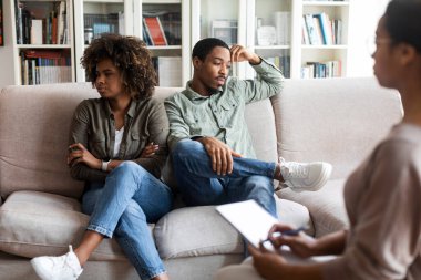 Tired of relationship, marriage problem. Upset frustrated african american millennial couple sitting on couch at marital therapists office, looking at different ways, copy space