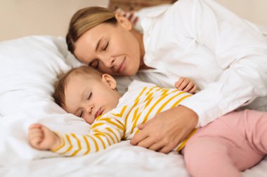 Peaceful mother and cute little child girl lying on bed, sleeping together with tranquility, mom embracing daughter during daytime sleep. Mother protection concept