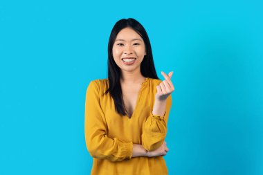 Positive Woman Showing Money Gesture. Portrait of Asian Positive Lady Smiling and Showing Give Me Money Gesture, Asking for Payment. Studio Shot Isolated on Blue Background, Copy Space
