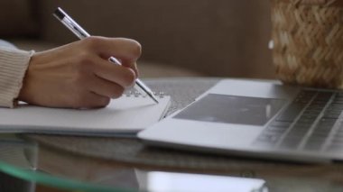 Online eğitim. Fotokopi kitabında tanınmayan bir kadın öğrencinin laptopta, yan görüntüde, boş alanda Webinar izlediği yakın çekim.