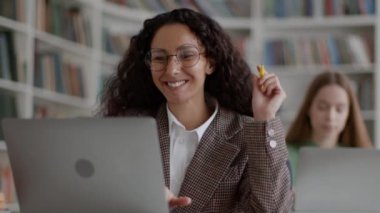 Başarılı bir eğitim projesi oldu. Gözlüklü mutlu genç bayan öğrenci laptopta sınav sonuçlarını okuyor ve bundan keyif alıyor, kütüphanede çalışıyor, izleme çekimi, yavaş çekim, serbest alan