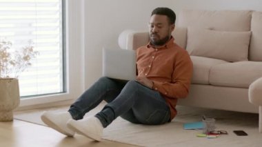 Internet connection problems. Young african american guy typing on laptop, feeling some discomfort, working distant from home, tracking shot, slow motion, free space