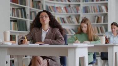Group of young smart ladies students writing notes in copy books, studying in college classroom, looking at teacher, free space