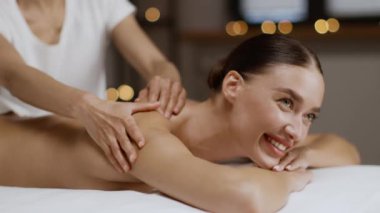 Healthy lifestyle and body care concept. Young and beautiful woman getting relaxing massage therapy at spa salon, lying on massage bed and smiling, slow motion, free space