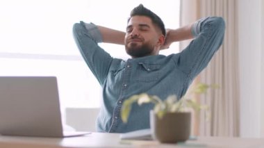 Successful project. Young happy middle eastern man employee finishing work on laptop and relaxing, feeling satisfied and glad, sitting at workplace, tracking shot, slow motion, free space