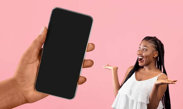 Surprised Young Black Woman Looking At Blank Smartphone In Huge Female Hand, Happy Excited African American Lady Enjoying New Mobile App While Standing Isolated Over Pink Background, Collage, Mockup