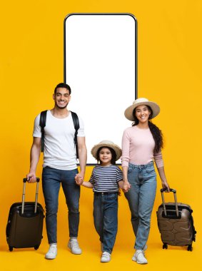 Üç kişilik mutlu bir Arap ailesi el ele tutuşuyor ve sarı stüdyo arka planında büyük bir telefonla çantalarla yürüyorlar, neşeli Orta Doğulu aileler ve küçük kızları tatile çıkmaya hazır.