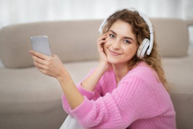 Favorite Leisure. Beautiful Young Woman Wearing Wireless Headphones Listening Music On Smartphone While Relaxing At Home, Closeup Shot Of Happy Woman In Earphones Enjoying Favorite Playlist