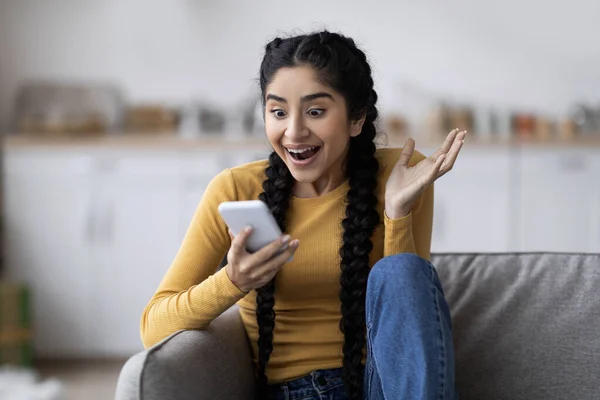 Excited Young Indian Woman Looking Smartphone Screen While Sitting Couch — Foto Stock