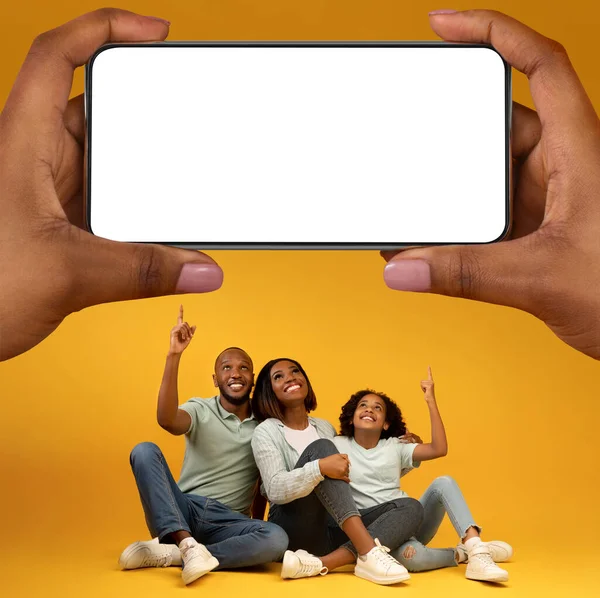 Look There. Happy Black Family With Daughter Pointing Above At Huge Blank Smartphone In Giant Female Hands, Cheerful African American Parets And Female Child Recommending Online Offer, Mockup