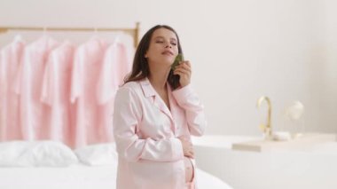 Anti edema procedures during pregnancy. Young pretty pregnant woman doing self massage with gouache stone, standing at home in morning, slow motion, empty space