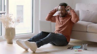 Comfortable freelance work. Young african american guy putting on headphones and typing on laptop, enjoying remote work and music at home, tracking shot, slow motion, free space