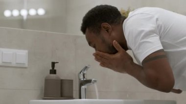 Personal hygiene habit. Young sleepy african american guy washing his face with water in morning, waking up at bathroom, slow motion, empty space