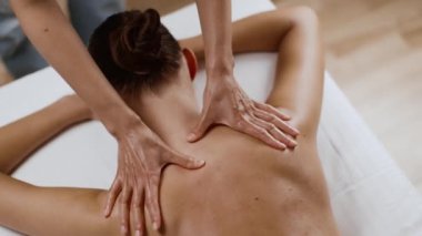 Alternative body healing. Top view of unrecognizable masseur hands massaging female neck and shoulders, young woman client lying on massage bed at salon, tracking shot, slow motion