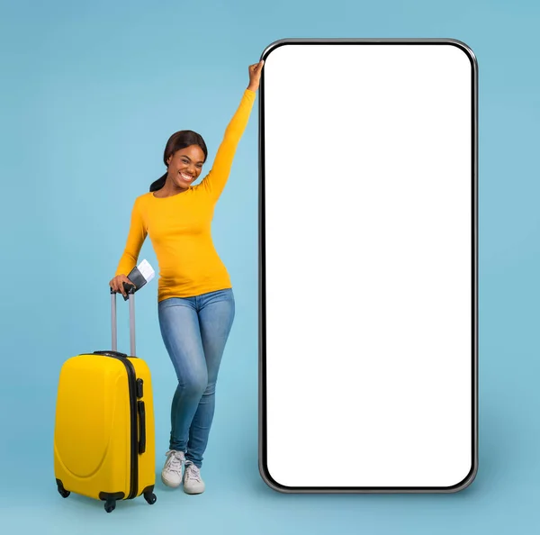 青いスタジオの背景 コピースペースの上にポーズスーツケース付き幸せな黒の女性旅行者の完全な長さの肖像画 女性の観光客チェック旅行オンライン提供 巨大な携帯電話で立っています モックアップ — ストック写真
