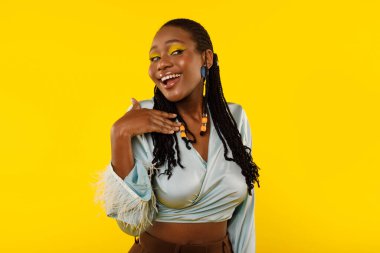 Gorgeous Black Woman With Bright Makeup Smiling Looking At Camera Posing Holding Hand Near Face Standing On Yellow Background, Studio Shot. Beauty And Style Concept