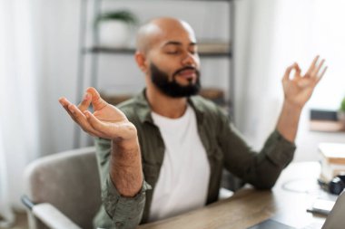 Relaxed latin man meditating in front of laptop and calming down, relaxing with eyes closed at workplace at home office. Online yoga, relaxation and mindfulness