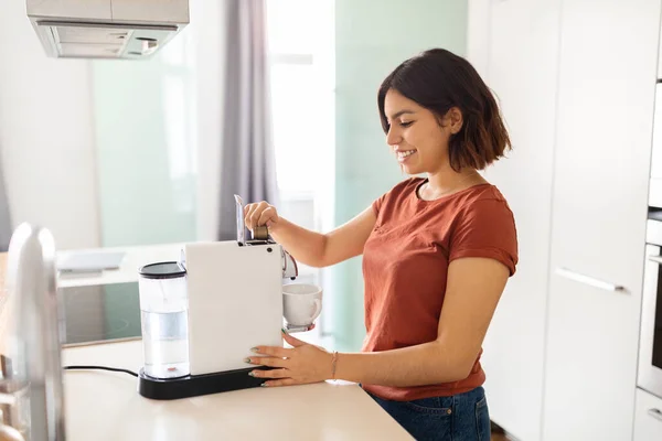 stock image Smiling Young Arab Woman Preparing Coffee With Modern Machine In Kitchen, Happy Middle Eastern Female Putting New Capsule While Making Caffeine Drink In The Morning At Home, Copy Space