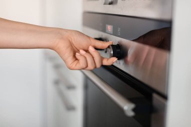 Unrecognizable Woman Turning Knob On Modern Oven In Kitchen, Young Female Adjusting Temperature On Electric Stove While Cooking At Home, Controlling Regime Of The Burner, Closeup Shot