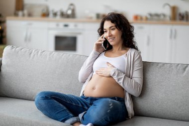 Portrait Of Beautiful Young Pregnant Woman Talking On Cellphone At Home, Smiling Expectant Lady Relaxing Couch In Living Room And Enjoying Pleasant Mobile Phone Conversation, Copy Space
