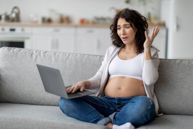 Stressed Pregnant Woman Having Problems With Laptop Computer At Home, Anxious Expectant Female Suffering Troubles With Internet While Working Online, Sitting On Couch In Living Room, Free Space