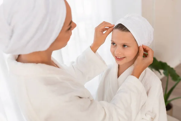Mom Adjusting Hair Towel Wrap For Her Little Daughter, Mother And Preteen Female Child Wearing Bathrobes Having Beauty Day At Home, Cute Kid Girl In Bath Cap Looking At Mother With Love, Closeup