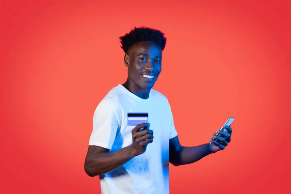 Wesoły Przystojny Młody Czarny Mężczyzna Korzystający Smartfona Pokazujący Kartę Kredytową — Zdjęcie stockowe