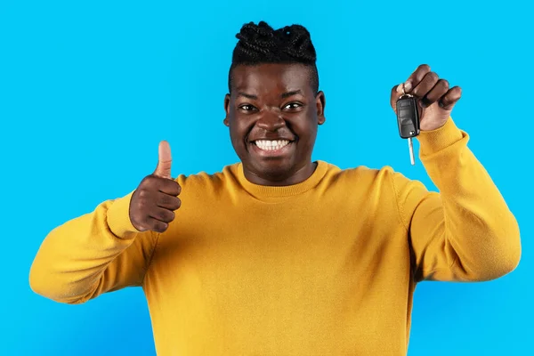 Car Rent. Joyful Black Man Holding Key And Showing Thumb Up While Posing Isolated On Blue Studio Background, Happy African American Male Recommending Rental Company Or Celebrating Buying New Auto