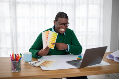 Gülümseyen Siyah Tasarımcı, iş yerinde oturan müşteriyle birlikte dizüstü bilgisayara renk şeması seçtiğini gösteren video çağrısı yapıyor. Başarılı Tasarım Kariyeri Konsepti