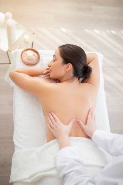 Relaxed indian woman enjoying back massage in spa salon, top view of professional female therapist doing therapeutic body treatment to attractive young lady in wellness center, above shot clipart