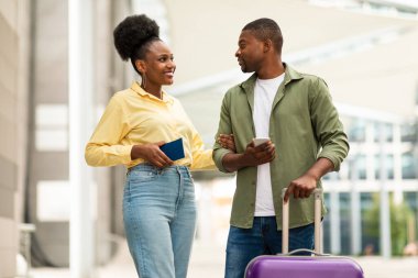 Gülümseyen Afro-Amerikan çift cep telefonu ve pasaportu dışarıda, havaalanı yakınlarında duruyor. Turizm ve Teknoloji, Seyahat Başvurusu Reklam Kavramı