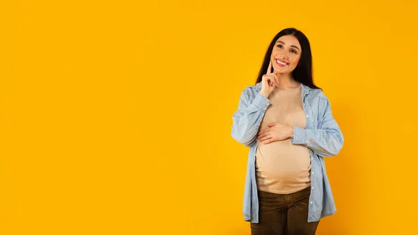 Šťastná Zamyšlená Těhotná Žena Vybírá Jméno Pro Dítě Pózuje Žlutém — Stock fotografie