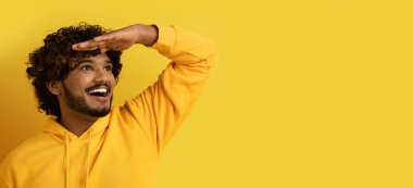 Güzel teklif. Şaşırtıcı derecede yakışıklı kıvırcık saçlı, kapüşonlu genç adam gözlerinin yanında el ele tutuşuyor, sarı stüdyo arka planındaki reklam için fotokopi alanına bakıyor, web pankartı.