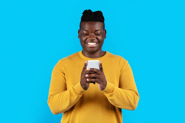 年轻黑人站在蓝色工作室的背景下使用现代智能手机 千年快乐非洲裔美国人与朋友在手机上或网上购物 复制空间 — 图库照片